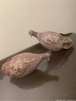 Side view of two ceramic dove sculptures resting on a dark wood surface, showing shape and feather texture