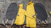 Two black Condar firewood totes laid flat on stone surface with yellow rain suit folded between them