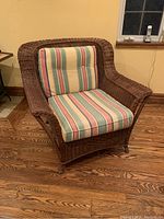 Front view of the wicker chair showing the striped back and seat cushions, curved armrests, and brown woven wicker frame.