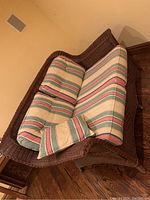 Top side angle showing brown wicker frame with striped seat and back cushions and matching throw pillow