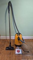 Full overview showing vacuum body, hose, wand, floor head, and replacement bag pack on hardwood floor
