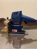 Side view of Ryobi Biscuit Joiner DBJ50 showing blue and black housing and clear adjustable base plate.