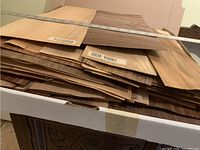 Stack of assorted wood veneer sheets partially inside a large pizza box with labels visible on some veneers.