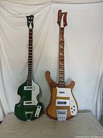 Photo of two wooden decorative wall guitars, one green with white and one natural wood with white and silver accents, displayed standing against a white backdrop.
