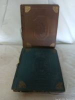 Two vintage scrapbooks, one brown and one blue-green, shown upright side-by-side on a white background.