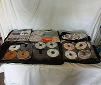 Four black music cases open and displayed side-by-side showing numerous CDs organized in transparent sleeves inside the cases.