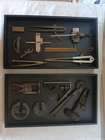 Two trays containing assorted vintage mechanist and measurement tools including dividers, calipers, and wrenches, shown for full lot overview.