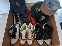 Box containing five pairs of men's athletic shoes in various colors and styles and four baseball-style hats placed on top.