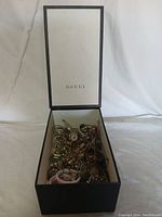 Open Gucci box showing mixed jewelry inside including bracelets, bangles, earrings, and chains.