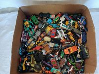 Box full of assorted toy cars of many colors and styles, including race cars, trucks, and vintage models, showing condition and variety.