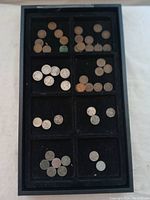 Top view of a black display tray with several compartments containing assorted pennies, nickels, and dimes.