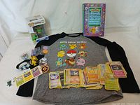 Full spread of the Pokemon items including cards, shirt, Funko Pop figure, handbook, wristband, pins, and keychain.
