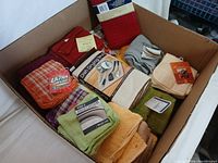 Box filled with assorted new bathroom textiles such as towels, washcloths, and mats in multiple colors.