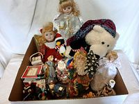 Photo of assorted Christmas dolls, figurines, and plush including Santa Claus, snowmen, angels, teddy bear, and penguin in a cardboard box