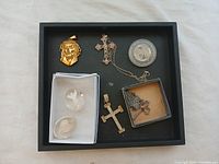 Overview of all 8 religious items display in black tray including crosses, blessing stones, medallion, and coin