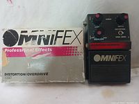 Photo of the MNIFEX Omni FEX 700D Distortion/Overdrive guitar pedal next to its original box, showing pedal surface and controls.