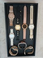 Top view of 8 pink watches laid flat in a tray showing various bands and dial designs including metal, leather, fabric bands.