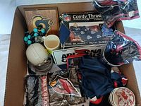 Sports memorabilia lot with NFL comfy throw, mini helmets, mugs, wooden plaques, and assorted sports-related items in a box