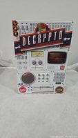 Front view of Decrypto board game box with retro cipher machine design