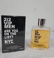 Photo of 2i2 VIP Men Eau de Parfum 100ml, bottle and box shown side by side on a white surface against a plain background. The box is black with white text and the bottle is clear with amber liquid inside, silver cap, and black text on front.