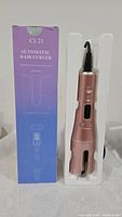 Automatic hair curler CI-21 in rose gold color next to its original box featuring product name; displayed in protective plastic insert, showing front view.