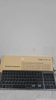 Creatmor wireless keyboard resting on its beige retail box with keyboard illustration and product name visible.