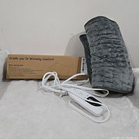Full view of body heating pad, white controller, and box in the background showing product and packaging.