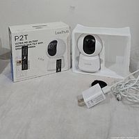 Photo showing camera, power adapter, white protective foam, and original box with product details.