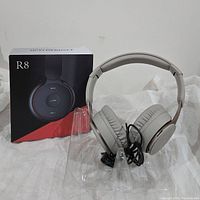 R8 Bluetooth headset in light gray with packaging box and charging cable on a display stand.