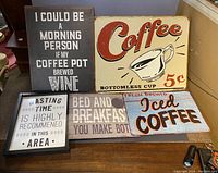 Five coffee and kitchen themed decorative signs arranged on a table showing text and coffee cup illustrations.
