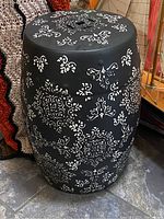 Side view of black metal plant stand with white stenciled floral and geometric patterns, showing cylindrical shape and height.