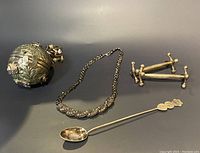 Photo showing all items: ornate round container, silver-tone necklace, pair of small stands, decorative spoon