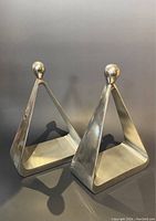 Pair of metal triangular bookends with spherical tops shown together on neutral background.