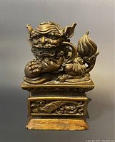 Front view of carved Foo Dog statue showing detailed face, curled mane, paw on ball, and carved base.