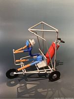 Side view of a colorful metal golfer figurine sitting in a white metal frame golf cart with red golf bag and clubs.