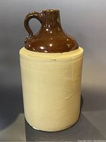 Front view of vintage demijohn jug showing beige lower body and brown glazed upper portion with handle.