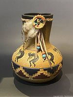 Front view of the First Nations earthenware vessel showing the painted black Kokopelli figures and geometric designs.