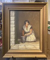 Framed oil painting showing a woman kneeling and working with a metallic vessel against stone walls.