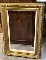 Full view of large gold ornate frame standing upright, shows overall design and size