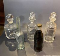 Lot of four glass bottles including two cut glass decanters with stoppers, one round clear glass decanter with stopper, and two vintage-style bottles, one with Coca-Cola content.