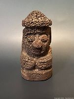 Front view of volcanic rock sculpture with carved face and hat feature