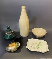 Photo showing five ceramic and decorative items including a tall bottle, small bowl, green lidded pot, and two dishes with floral decorations.