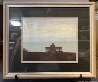 Full framed artwork showing the seated figure silhouette by water at sunset with silver frame and matting.