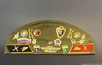 Olive-green side cap with multiple metal pins arranged in two rows across the front.