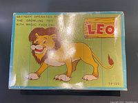 Photo of the front of the box showing a stylized cartoon lion, product name 'Leo' and text stating it is a battery operated mechanical pet with magic face-change.