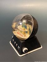 Side view of vintage New York City snow globe illustrating the miniature NYC skyline inside a clear dome mounted on a black base with a white knob.