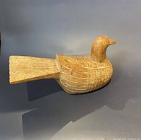 Side view of the wooden carved bird sculpture showing detailed wing and tail patterns.
