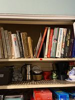 Shelf with assorted cookbooks including Jamie Oliver and others, alongside kitchen items such as coffee makers and a recipe box.