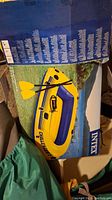 Box showing the fully assembled yellow and blue Intex Challenger 2 inflatable boat with two yellow oars crossed inside.
