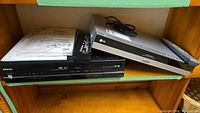 Side view of Toshiba VCR/DVD combo and LG DVD player with remotes and manuals on shelf